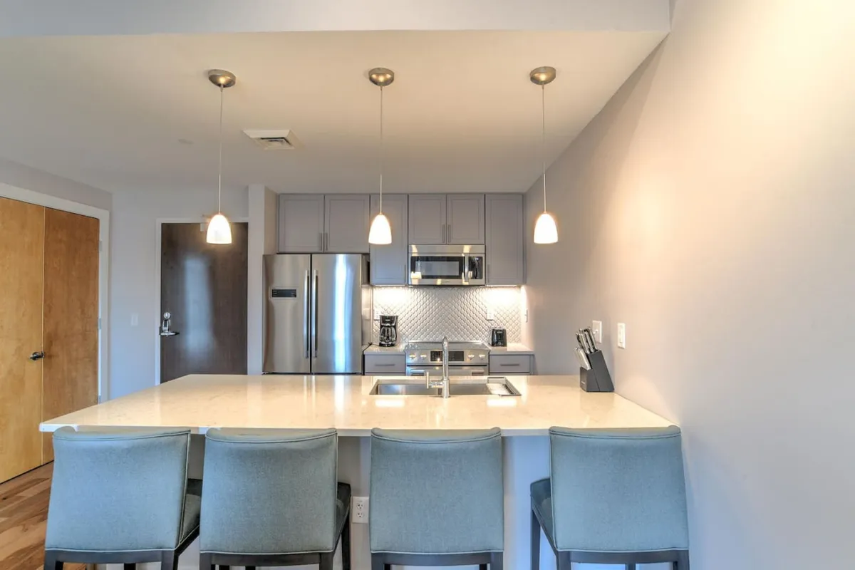 A spacious, contemporary kitchen featuring a large island with seating, stainless steel appliances, and elegant pendant lighting. The countertop is expansive, and the setting exudes a welcoming vibe ideal for both meal prep and casual gatherings. The space is staged with hints of activity, such as baking cookies, which makes it feel inviting and lived-in.