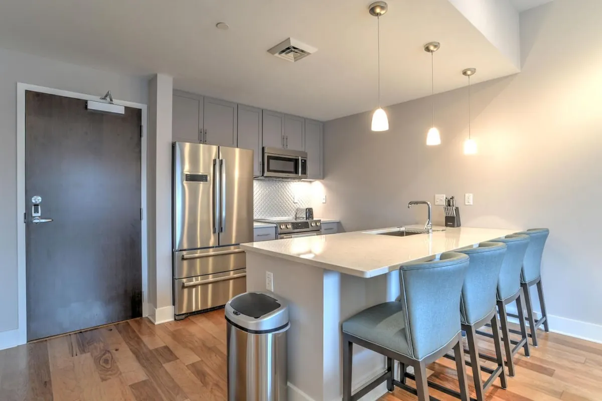 A modern kitchen and dining area with a prominent island, sleek stainless steel appliances, and warm, contemporary lighting. The table is set for entertaining, suggesting the space’s readiness for hosting dinners or sharing recipes, aligning with the multifunctional use described in the section.