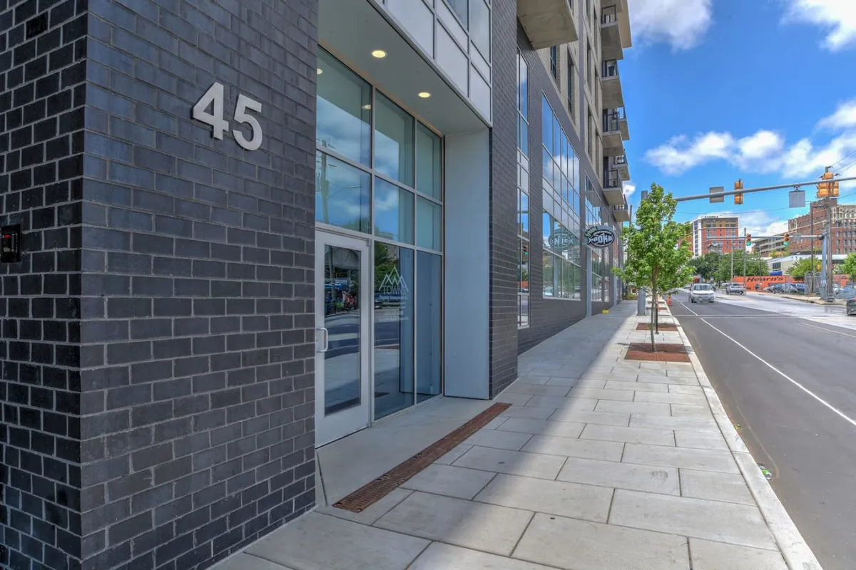 An exterior shot of the building facade, highlighting large glass windows and the entrance marked with the number 45. People are seen walking and engaging with the vibrant street scene, suggesting close proximity to cafés, shops, and the lively downtown area.