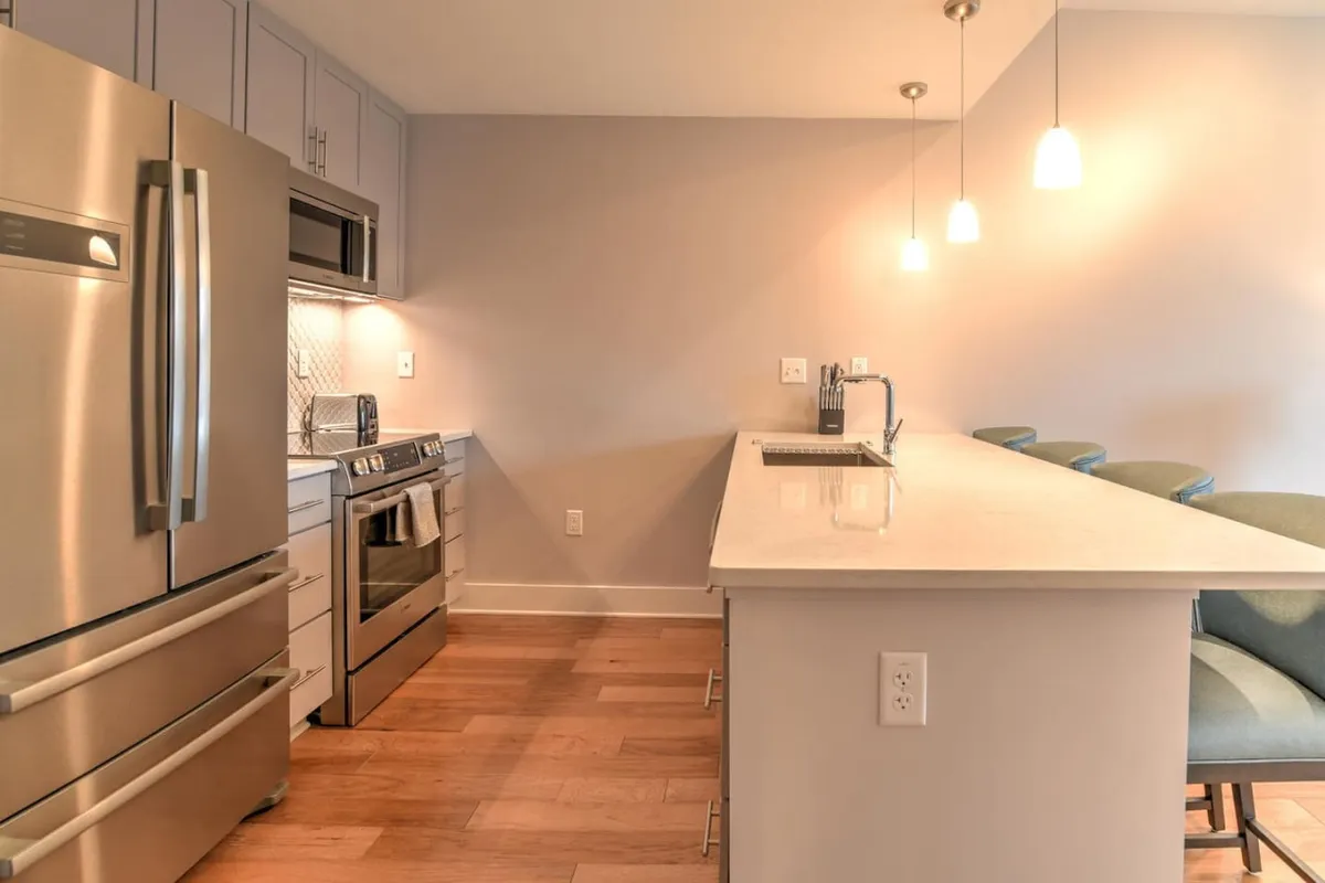 A contemporary kitchen scene with a central island, stainless steel appliances, pendant lighting, and visible space for both cooking and casual dining. The modern, functional layout highlights opportunities for culinary experimentation and communal dining.